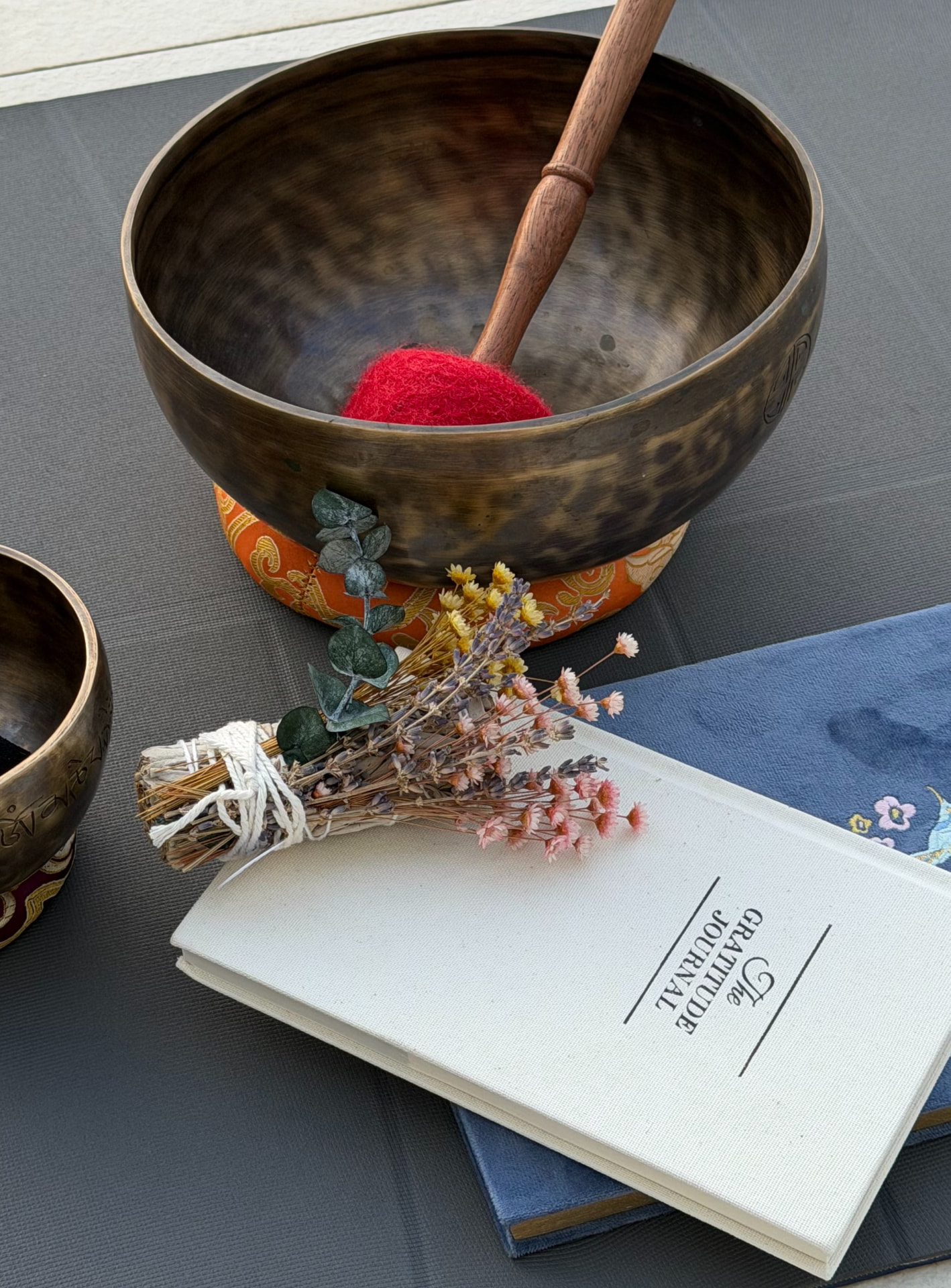 A gratitude journal beside brass singing bowls and dried flowers