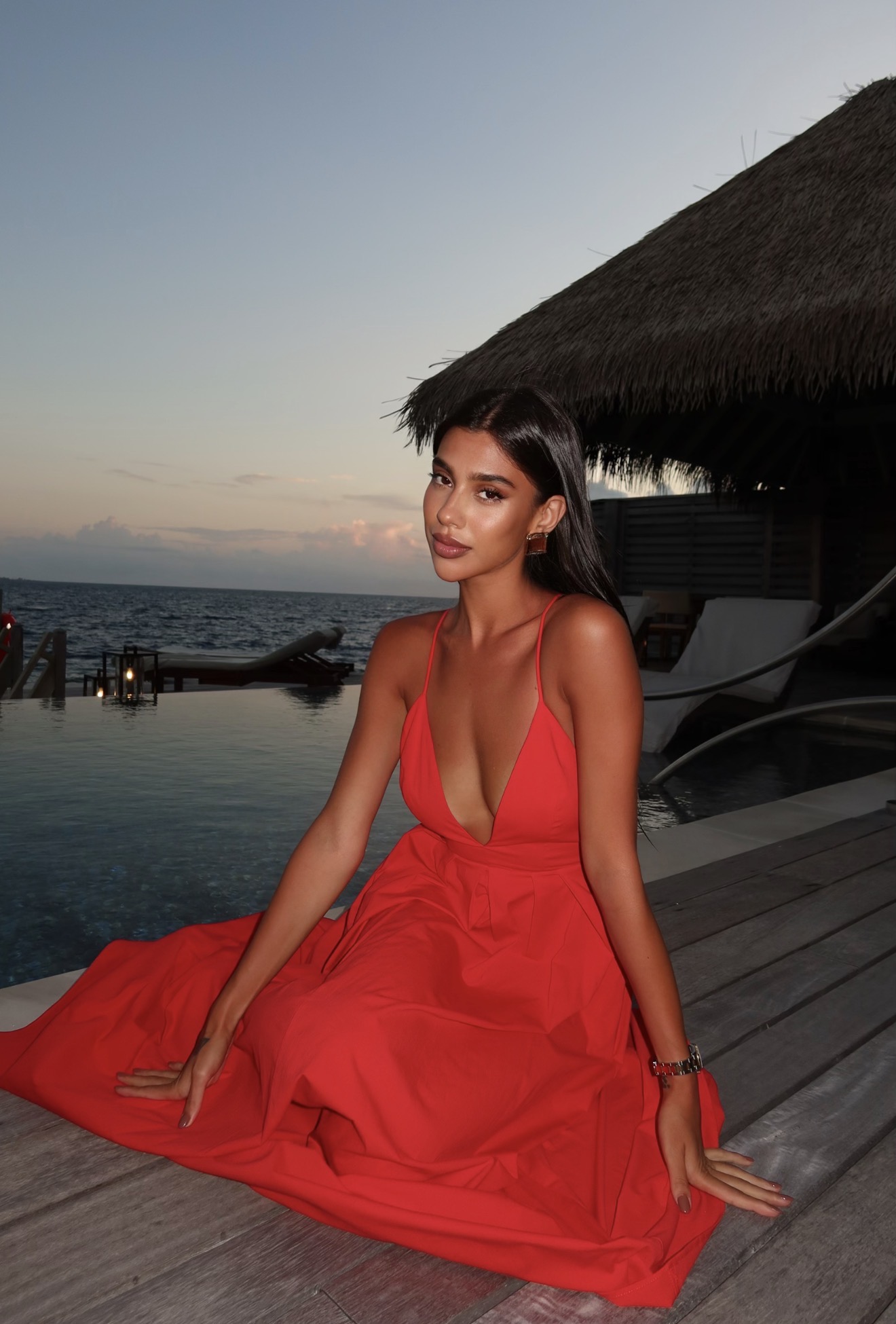 Shabi sitting by the water at dusk in a red dress