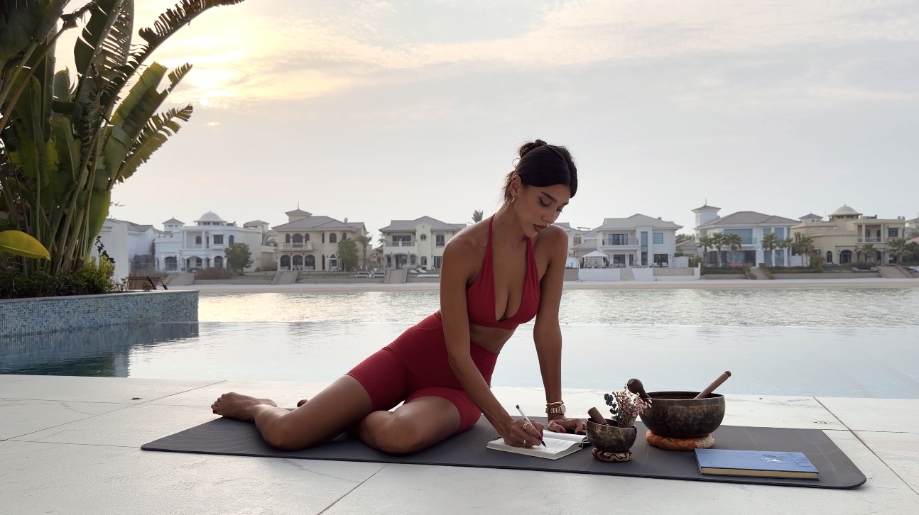 Shabi writing in her journal beside the water at sunset